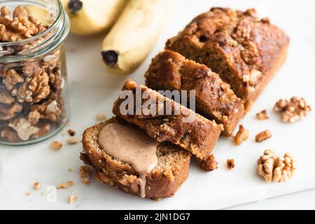 Veganes Bananenbrot mit in Scheiben geschnittenen Walnüssen auf einem Marmorbrett, Nahaufnahme Stockfoto