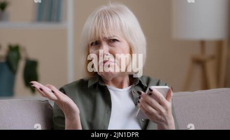 Frustrierte ältere Dame kaukasische ältere Frau mit Telefon liest schlechte Nachrichten in Handy-Nachricht traurig verärgert Schock Scheitern mit Smartphone-App. Besorgt Stockfoto