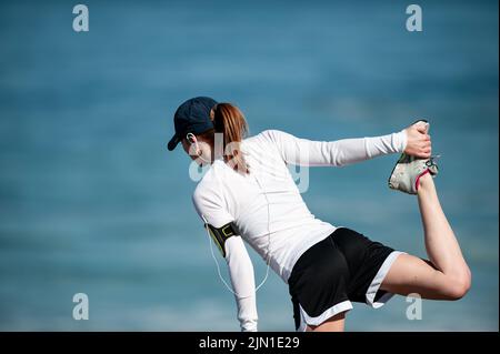 Das Bild einer Frau, die sich vor ihrem morgendlichen Strandlauf streckt. Nächstplatzierter Wärmt Sich Auf, Beach Runner, San Francisco, Kalifornien, Gesundheit, Wellness, Sport Stockfoto