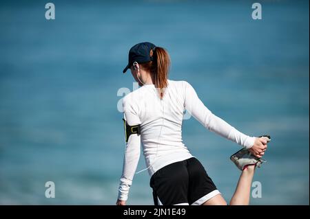 Das Bild einer Frau, die sich vor ihrem morgendlichen Strandlauf streckt. Nächstplatzierter Wärmt Sich Auf, Beach Runner, San Francisco, Kalifornien, Gesundheit, Wellness, Sport Stockfoto