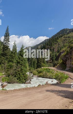 Ein wunderschöner stürmischer Gebirgsfluss von milchigem Farbton fließt schnell zwischen großen Steinen und Felsbrocken in der Nähe der Berge und des blauen Himmels. Der Gebirgsfluss f Stockfoto