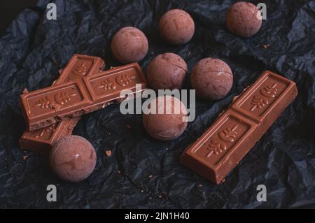 Schokoladen-Bonbons mit Schokoladenstücken auf dunklem zerknittertem Bastelpapier mit Lavendelblüten Stockfoto