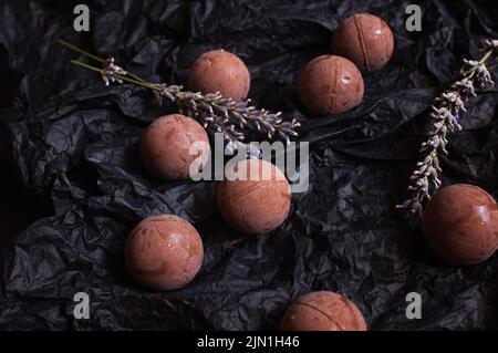 Schokoladen-Bonbons auf dunklem zerknittertem Bastelpapier mit Lavendelblüten Stockfoto