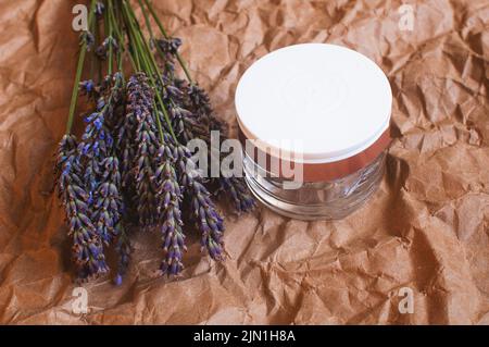 Glas Creme mit einem Bouquet von duftenden frischen Lavendelblüten auf einem Hintergrund aus braunem Kraftpapier Stockfoto