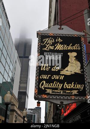 Das Schild für Lou Mitchell's, ein Restaurant, das 1923 in Chicago, IL, eröffnet wurde, ist in der Nähe des nebelverdunkelte Willis Tower (ehemals Sears Tower) abgebildet. Stockfoto