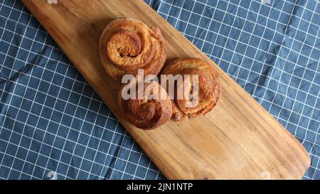 Ein Flatlay von drei hausgemachten Zimtbrötchen auf einem Holzbrett Stockfoto