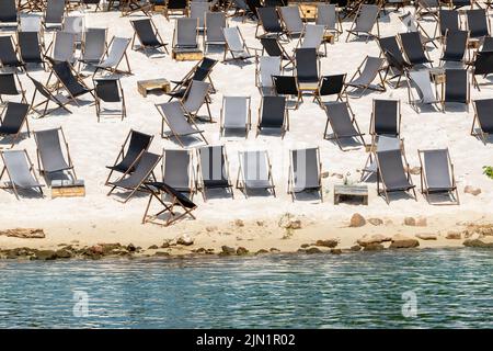 Landschaftlich schöner Blick auf das Wasser von vielen leeren schwarzen Holzliegen auf dem Sandfluss oder dem Meeresstrand. Reihen von Liegestühlen an geschlossener Küste aufgrund von Kontamination Stockfoto