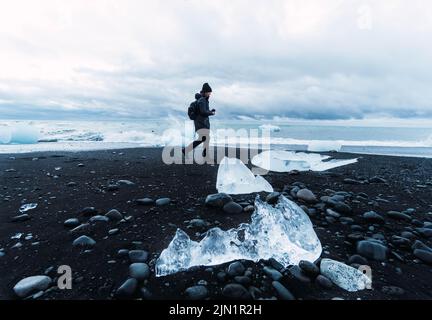 Person am schwarzen Strand, umgeben von Eisstücken Stockfoto