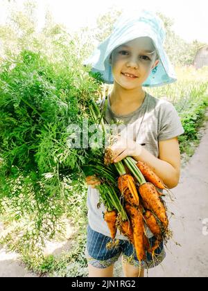 Nettes junges Mädchen mit Karotten im Garten an einem Sommertag Stockfoto