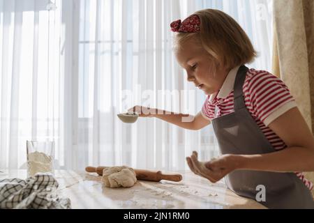 Das Mädchen in der Küche kocht aus Teig und Mehl. Stockfoto