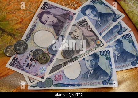 Münzen und Papierbanknoten des japanischen Yen auf dem Hintergrund des nationalen Gewebes mit Stickerei Stockfoto