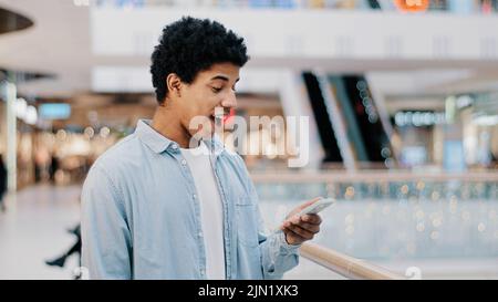Afrikanischer Dominikaner überrascht, als die Telefonnummer klingelt und auf den Bildschirm schaut, der einen unerwarteten Anruf entgegennimmt und lächelt und glücklich lacht Stockfoto