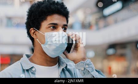 Nahaufnahme afroamerikanischer Kerl in medizinischer Gesichtsschutzmaske Gespräch Handy Anruf Annahme Gespräch mit Arzt Remote beschweren über Stockfoto