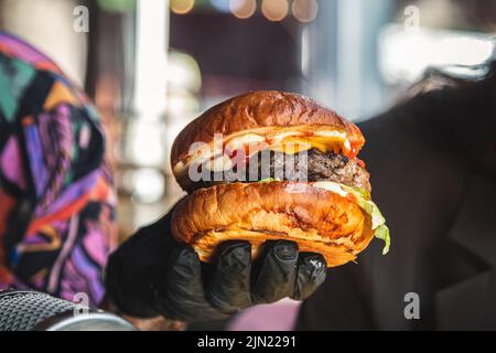 Appetitlich großer Burger in männlichen Handschuhen. Stockfoto