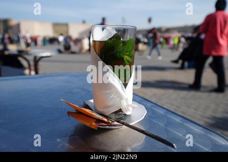 Traditioneller heißer marokkanischer Minztee mit Minzblättern in einem Glas, das mit einem Tuch auf einem Tisch verpackt ist. Marrakesch, Marokko. Stockfoto