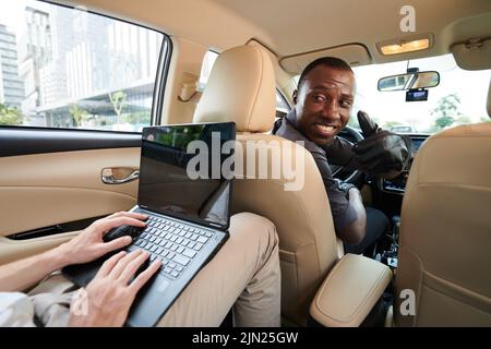 Der Taxifahrer wandte sich an den Passagier, der am Laptop arbeitete und den Daumen nach oben zeigte Stockfoto