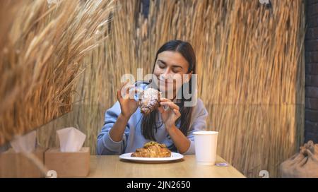 Eine junge Frau isst Croissants mit Kaffee in einem Café. Stockfoto