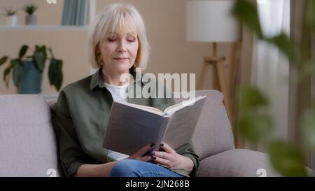 Allein kaukasisch 50s Dame kaukasisch alte Frau ältere Dame Senior Großmutter Professor Lehrer sitzen auf Sofa ruhen Studium Bildung entspannen an Stockfoto