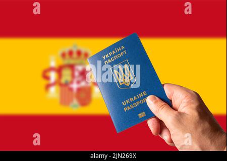 Ukrainischer biometrischer Pass in der Hand einer Frau vor dem Hintergrund der spanischen Nationalflagge. Reisen, Tourismus, Wirtschaft, Krieg in der Ukraine, Zuflucht Stockfoto