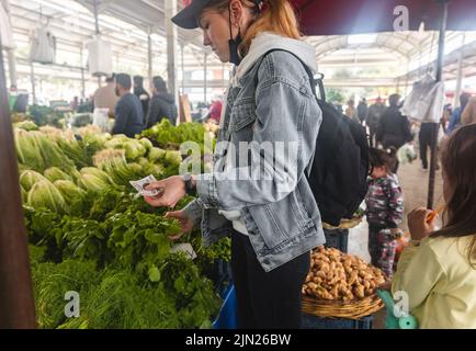 Kauf von frischen Bio-Produkten auf dem Bauernmarkt. Eine Frau wählt auf einem Lebensmittelmarkt frische Kräuter, Gemüse und Früchte. Stockfoto