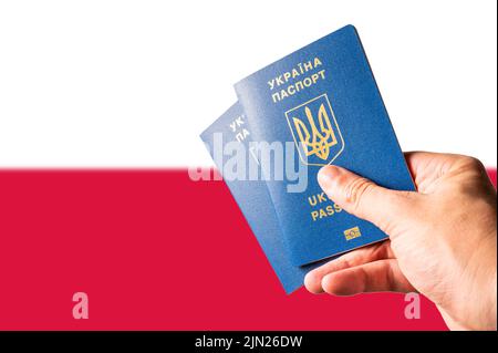 Zwei biometrische ukrainische Pässe in der Hand eines Mannes vor dem Hintergrund der polnischen Nationalflagge. Reisen, Tourismus, Flüchtlinge, Krieg in der Ukraine, BU Stockfoto