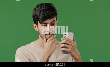Porträt Nahaufnahme arabischen jungen Mann im Studio auf grünem Hintergrund halten Telefon glücklich lächelnden Kerl Browsing sozialen Netzwerken Machen Sie online bestellen Nachrichten lesen Stockfoto