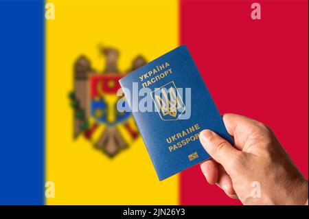 Ukrainischer biometrischer Pass in der Hand einer Frau vor dem Hintergrund der Nationalflagge der Republik Moldau. Tourismus, Wirtschaft, Reisen, Krieg in der Ukraine, Refu Stockfoto