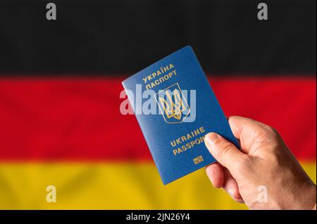 Ukrainischer Pass in der Hand einer Frau vor dem Hintergrund der deutschen Nationalflagge. Identifikation, Reisen, Geschäft, Auswanderung, Flucht aus Stockfoto