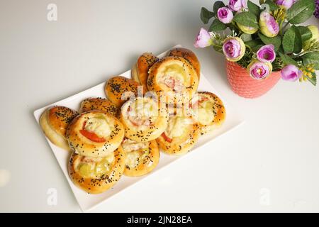 Frisch gebackene, sortierte Brötchen mit einer Füllung in einem weißen Teller auf dem Tisch. Stockfoto