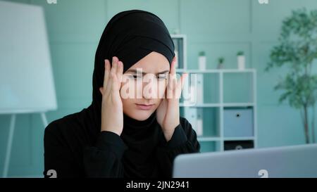 Müde arabische muslimische islamische Frau in schwarzen Hijab Arbeiterstudentin kurze Pause in der Online-Arbeit Gefühl Kopfschmerzen leiden mit Schmerzen Schmerzen Stockfoto