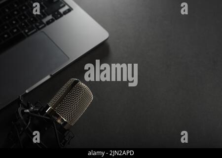 Auf einem dunkelgrauen Hintergrund, einem Studiomikrofon und einem Laptop. Low-Angle-Ansicht. Heimbüro. Heimmusik-Studio, Blogging, Radio, Journalismus, Streaming. T Stockfoto