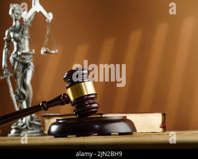 Urteilsvermögen und Gerechtigkeit. Ein hölzerner Gavel eines Richters, ein offenes Buch - die Verfassung und eine bronzene Figur der Göttin der Gerechtigkeit - Themis auf einem beigen b Stockfoto