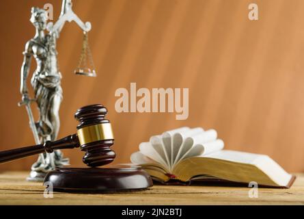 Symbole eines fairen Prozesses. Ein offenes Buch - die Bibel, ein hölzerner Gavel eines Richters und eine Bronzefigur von Themis - der Göttin der Gerechtigkeit auf einem beigefarbenen Rücken Stockfoto
