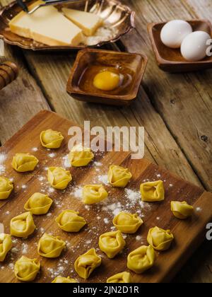 Der Prozess der Herstellung von Knödeln mit Fleischfüllung. Auf einem hölzernen Tisch stehen Knödel auf einem Schneidebrett, das mit Mehl und Zutaten bestreut ist. Niedriger Winkel Stockfoto