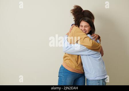 Glückliche Teenager-Mädchen in Jeans und Hoodies umarmen sich gegenseitig, um Liebe auszudrücken Stockfoto