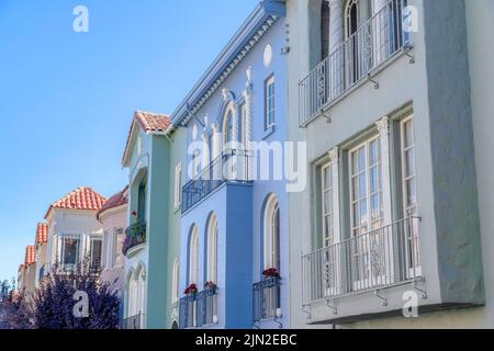 Gemalte Häuserzeile mit Fenstergeländern an der Vorderseite in San Francisco, CA. Es gibt einen Baum auf der linken Seite mit violetten Blättern in der Nähe der Häuser auf der ri Stockfoto