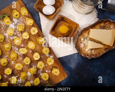 Appetitliche Ravioli auf einem Schneidebrett, Zutaten auf dunkelblauem Marmorboden. Der Prozess der Herstellung italienischer Ravioli. Viele Objekte. Es gibt sie Stockfoto