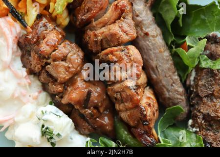 Teller mit Braai-Fleisch und Salaten. Dazu gehören Hühnerkebabs, Boerewors-Wurst, Lammkoteletts, Kartoffelsalat, Krautsalat und Curry-Nudelsalat Stockfoto