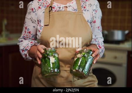 Nahaufnahme von zwei Gläsern mit eingelegten Gurken in den Händen einer Hausfrau und Präsentation von Konserven vor der Kamera Stockfoto