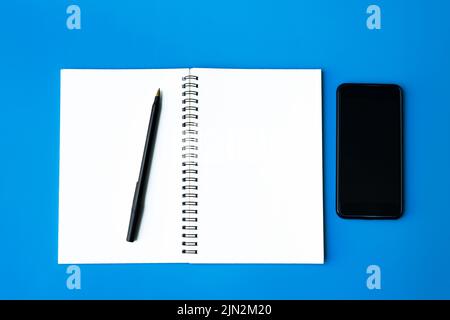 Ansicht von oben von Smartphone, Stift und Notizblock auf blauem Hintergrund. Speicherplatz kopieren. Stockfoto
