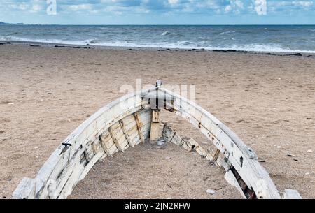 Bug eines alten verlassenen Holzbootes, das an einem Tag an einer leeren Sandküste liegt Stockfoto