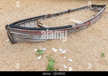 An einem Tag liegt ein altes verlassene Holzboot an einer leeren Sandküste Stockfoto