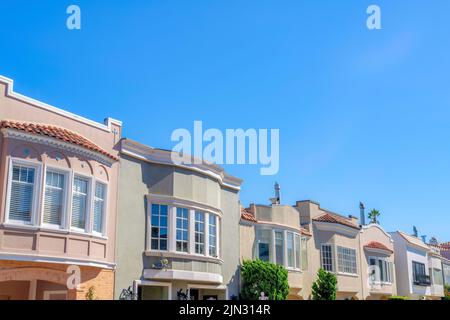 Reihe von bemalten Häusern mit Bogenfenstern und Ziegeldächern in San Francisco, CA. Außenansicht von Häusern mit Schächten gegen den klaren blauen Himmel und Blick o Stockfoto