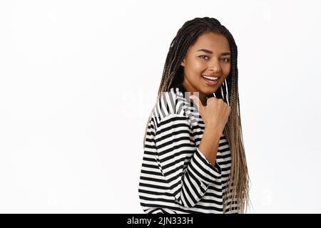 Porträt einer lächelnden afrikanischen Frau, die nach links zeigt, Logo oder Werbeangebot zeigt, Zeichen vorführt, in legerer Kleidung auf weißem Hintergrund steht Stockfoto