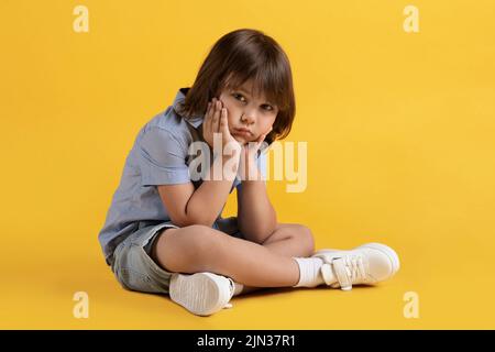 Trauriger, unglücklicher kleiner Junge, der auf dem Boden sitzt und allein leidet, sein Kinn auf die Hände lehnt, die Kamera anschaut, freien Raum Stockfoto