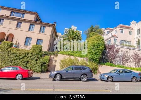 Holländische Winkelaufnahme eines Viertels mit schrägen Häusern in San Francisco, CA. Vorne gibt es eine flache Straße mit geparkten Fahrzeugen gegen die große Stockfoto