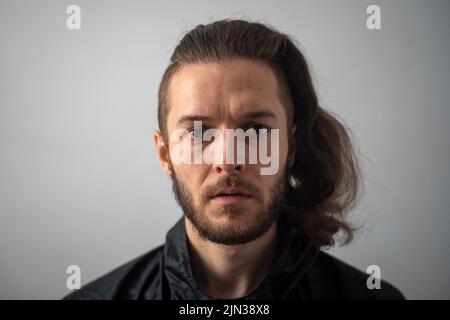 Junger weißer Mann mit Bart und langem Haar, der die Kamera anschaut Stockfoto