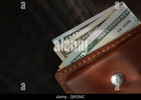 Nahaufnahme von hundertzehn-Dollar-Banknoten in brauner Ledertasche auf schwarzem Hintergrund Stockfoto