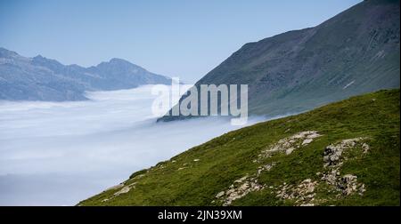 Ein riesengroßes, kreisförmiges Tal, umgeben von hohen Bergen, dem Cirque de Troumouse (Pyrenäen), Wolken, die das Tal füllen, und einem klaren, blauen Sommerhimmel Stockfoto