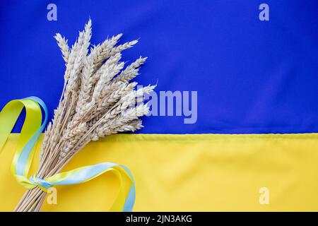 Bouquet von goldenen Weizenohren mit einem gelben und blauen Band auf der Flagge der Ukraine Hintergrund gebunden. Unabhängigkeitstag der Ukraine, Tag der Verfassung, FLA Stockfoto